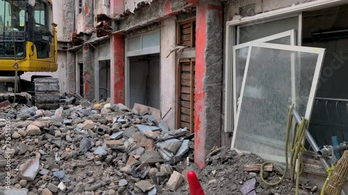 Demolition site of an old house, with an excavator on top of rubble in the middle of the gutted building with no roof or inner structure, panning from right to the center where the excavator is. photo