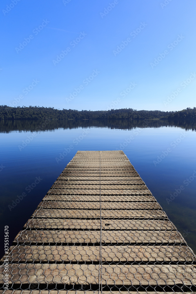 Wooden pier in the morning at calm mirror lake with mountain background in New Zealand.