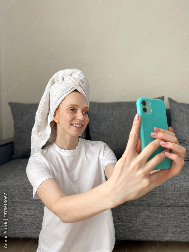 young woman with a towel on her head takes a selfie with her smartphone at home. young woman with a towel on her head takes a selfie with her smartphone at home.