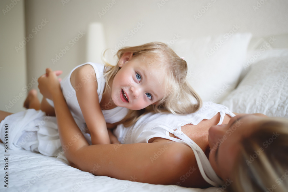 young woman hugging with her daughter on a white bed young woman hugging with her daughter on a white bed