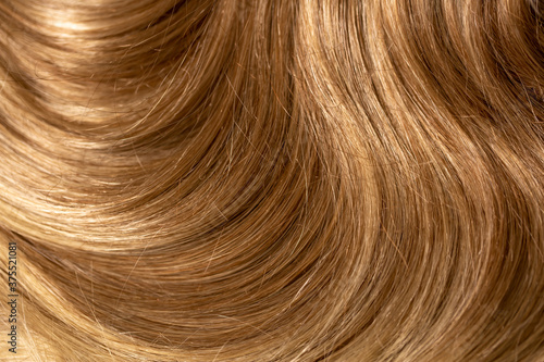 Background hair light brown closeup. Female long blond hair close-up as a background. Beautifully laid wavy shiny curls.Hair coloring. Hairdressing procedures. Copy space with space for text.