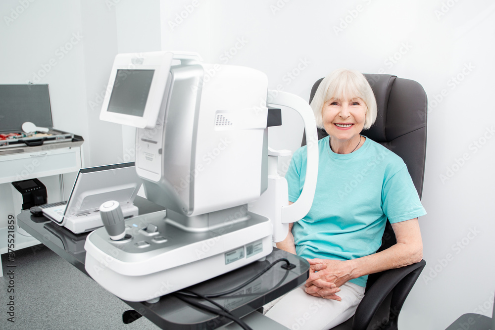 Smiling old woman checking eyesight in a clinic using diagnostic ophthalmic equipment. Eye exam of the elderly people Smiling old woman checking eyesight in a clinic using diagnostic ophthalmic equipment. Eye exam of the elderly people