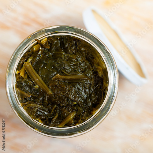 Canned green spinach in opened glass jar on wooden surface, nobody