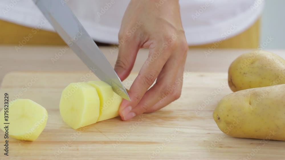 woman is slicing potato on wooden cutting board woman is slicing potato on wooden cutting board