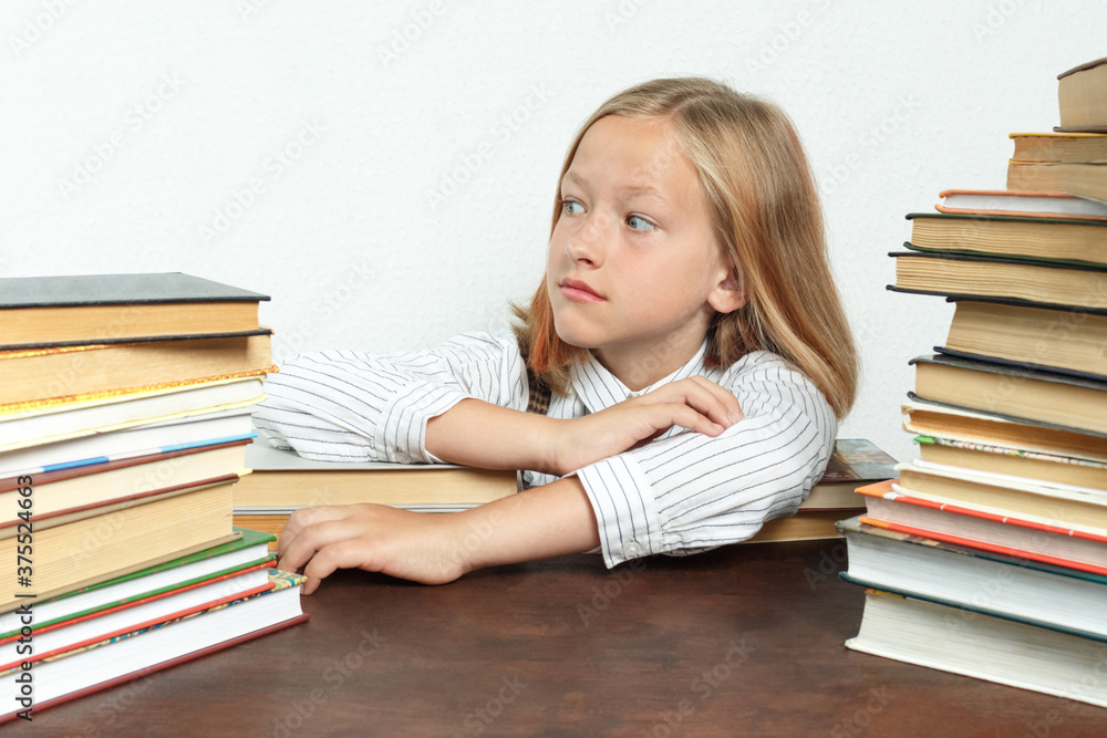 Portrait of a teenage girl who sits at a table among the books and looks to the side. Isolated background. Portrait of a teenage girl who sits at a table among the books and looks to the side. Isolated background.