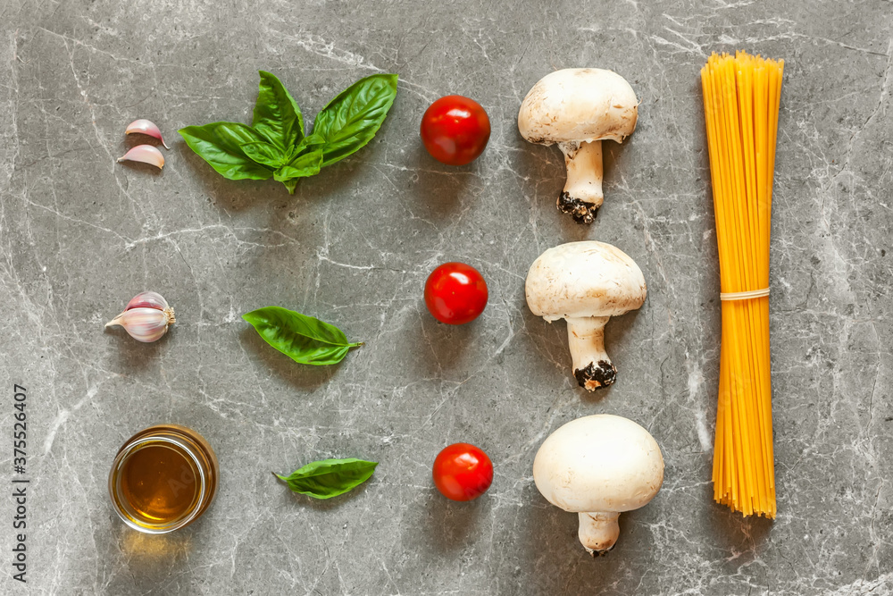 Top view of ingredients for pasta with mushrooms: spaghetti, basil, garlic,cherry and olive oil on gray stone background Top view of ingredients for pasta with mushrooms: spaghetti, basil, garlic,cherry and olive oil on gray stone background