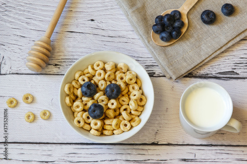 Honey rings with blueberries and milk in a bowl on the wooden background. Copy space. Top view. Flat lay. Horizontal orientation.