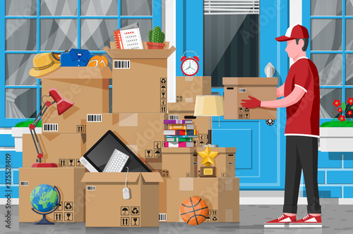 Moving to new house. Family relocated to new home. Male mover, paper cardboard boxes near house facade. Package for transportation. Computer, lamp, clothes, books. Vector illustration in flat style