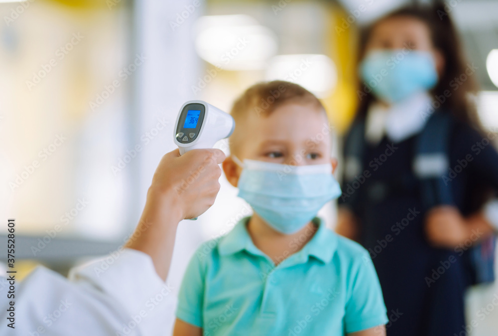 Temperature screening and medical check at school. Child in face mask in class in covid-19 outbreak. Teacher with thermometer at preschool entrance. Temperature screening and medical check at school. Child in face mask in class in covid-19 outbreak. Teacher with thermometer at preschool entrance.