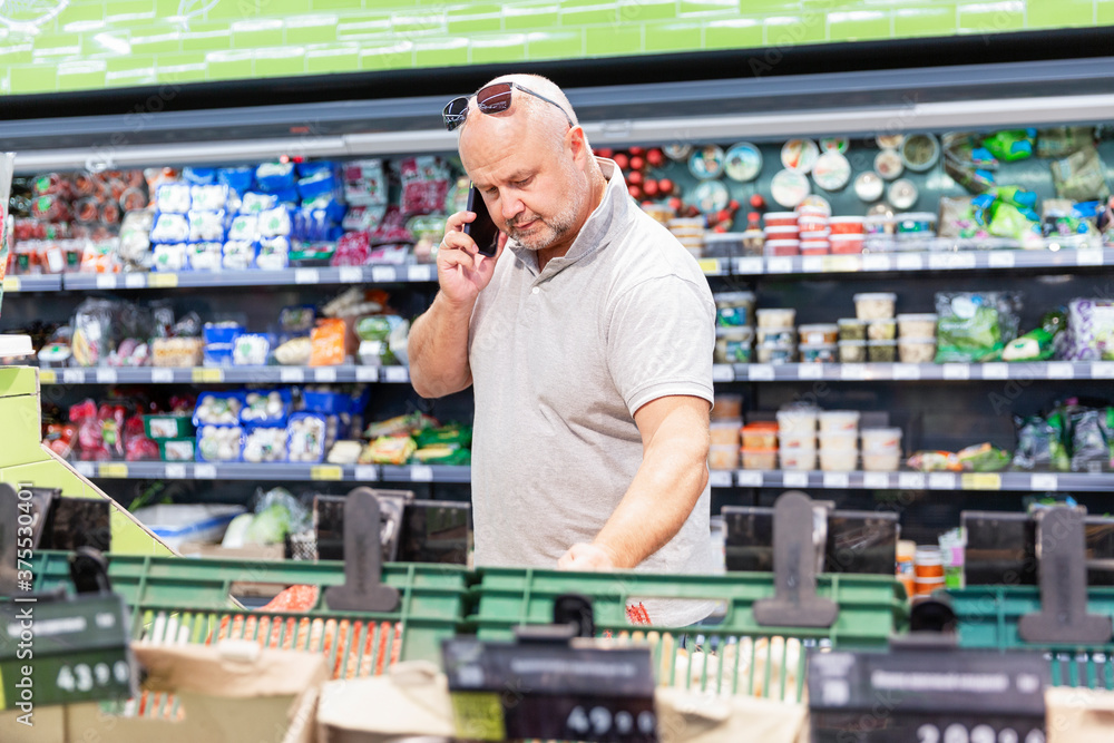 A man in a grocery store with a phone. Large selection of products.