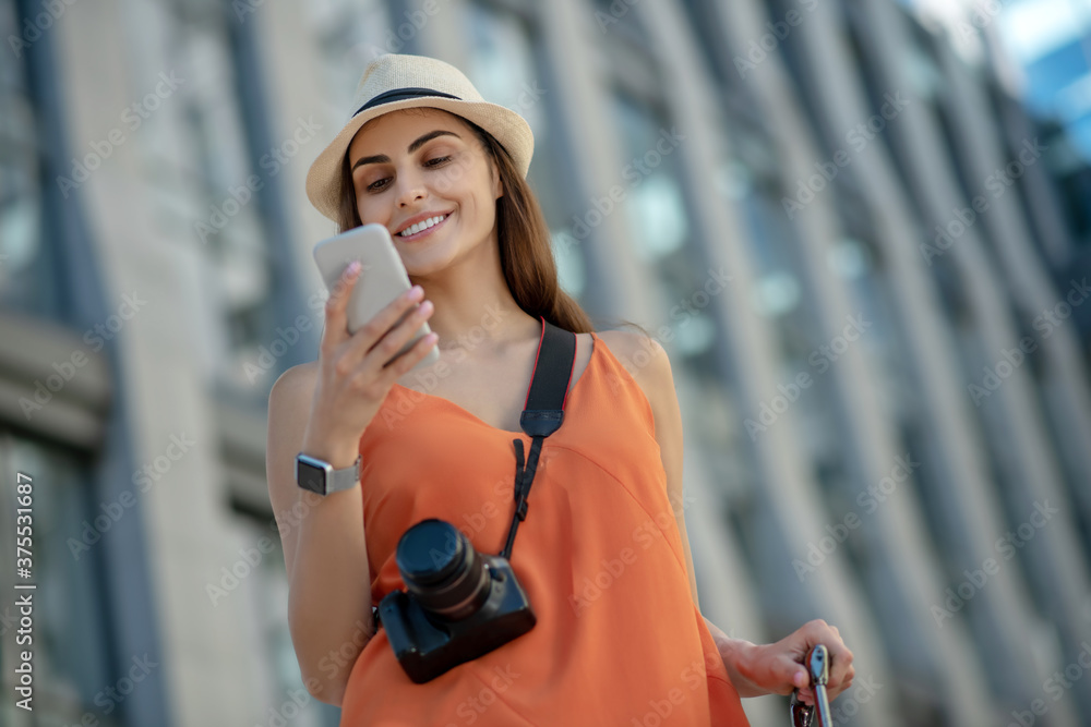 Dark-haired young woman in a hat holding smartphone and reading