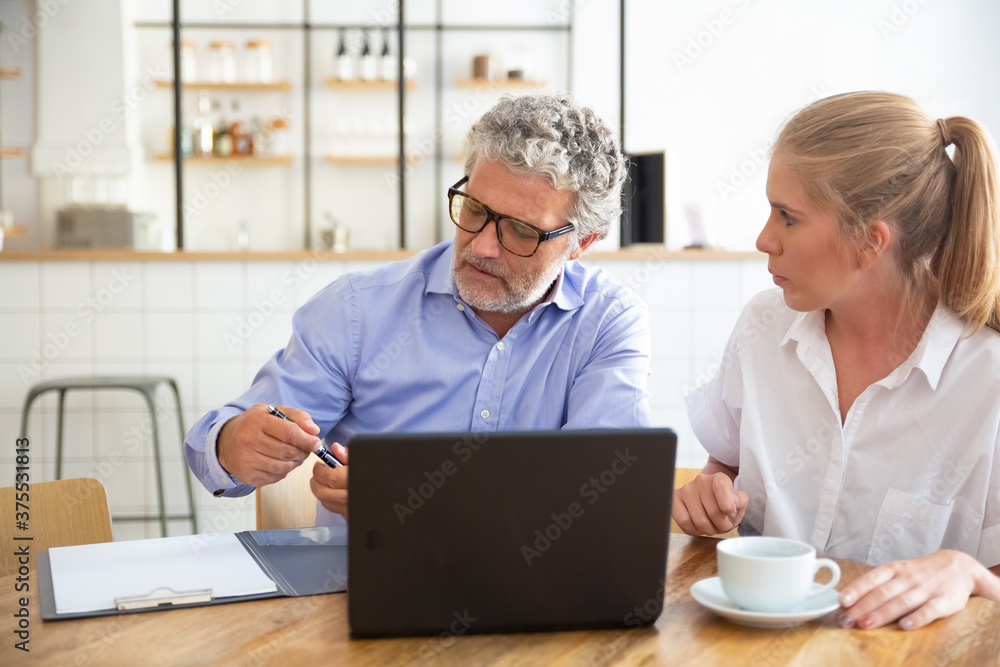 Businessman meeting with female agent at co-working, sitting at open laptop, taking pen for signing agreement. Medium shot. Consulting or cooperation concept Businessman meeting with female agent at co-working, sitting at open laptop, taking pen for signing agreement. Medium shot. Consulting or cooperation concept