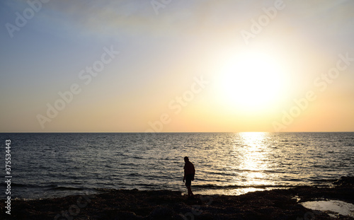 In the evening at sunset, a lonely man walks by the sea on the beach