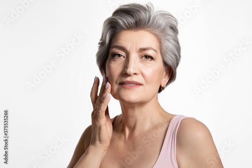  Old beautiful lady touching cheek with hand, enjoying perfect appearance. Skincare, cosmetology