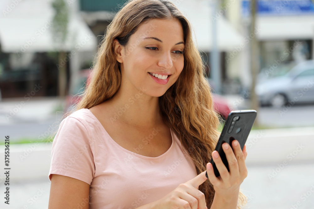 Portrait of a beautiful smiling Brazilian woman using mobile phone in city street