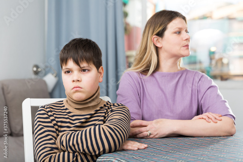 Offended son sitting at tablr after quarrel with mother in domestic interior photo