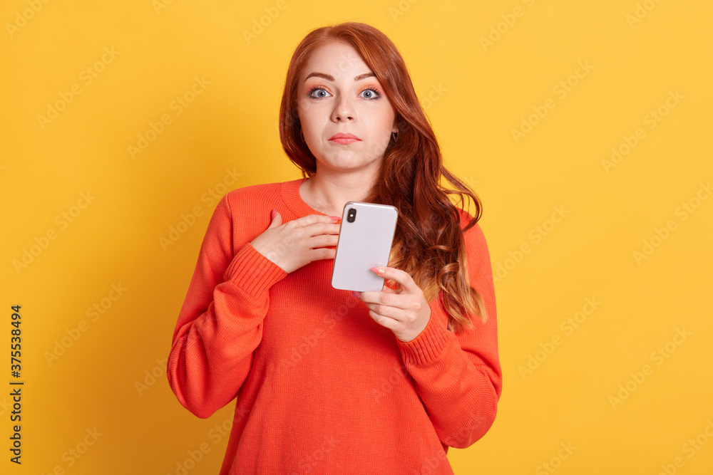 Shocking news! Close up portrait of surprised young woman in orange casual sweater reading sensational news on smart phone, has astonished facial expression. Shocking news! Close up portrait of surprised young woman in orange casual sweater reading sensational news on smart phone, has astonished facial expression.