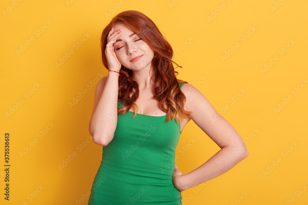 Portrait of beautiful redhead tired girl posing with closed eyes, wearing green shirt, touching her head, having headache, red haired lady suffering from pain. Portrait of beautiful redhead tired girl posing with closed eyes, wearing green shirt, touching her head, having headache, red haired lady suffering from pain.