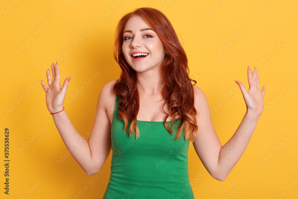Portrait of young stunning model with bright red hair, pretty woman in fashionable green shirt, posing with excited facial expression isolated over yellow background. Portrait of young stunning model with bright red hair, pretty woman in fashionable green shirt, posing with excited facial expression isolated over yellow background.