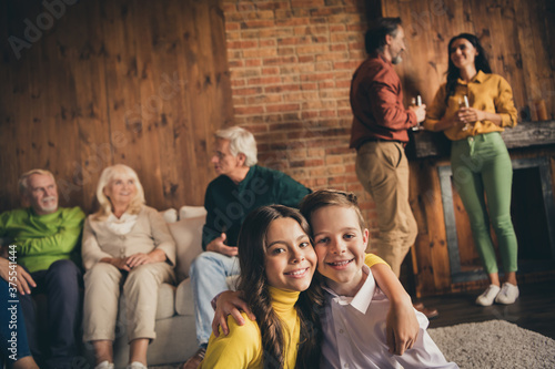 Photo of full family seven people gathering two little kids embrace grandparents communicate parents drink sparkling wine sitting sofa generation in home evening living room indoors