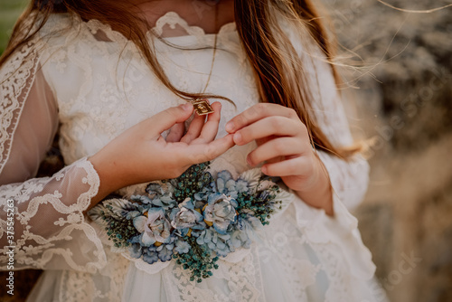 A girl dressed for a first communion holding in her hands a  virgin medal 