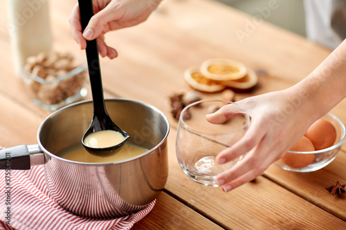 christmas and seasonal drinks concept - close up of hands with ladle pouring eggnog from pot to glass at home photo