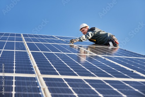 Side view of male worker installing solar modules and support structures of photovoltaic solar array. Electrician wearing safety helmet and gloves while working with solar panel. Concept of sun energy