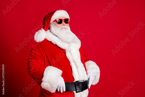 Photo of retired old man grey beard hands belt self-assured prepare save christmas eve spirit protector wear santa costume gloves coat sunglass headwear isolated red color background