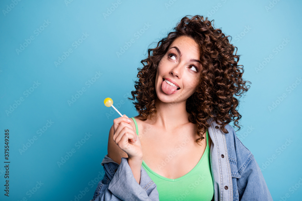Obraz premium Photo of funny girl youth hold lollipop look copyspace think thoughts imagine tasty yummy dessert show tongue out wear green tank-top isolated over blue color background