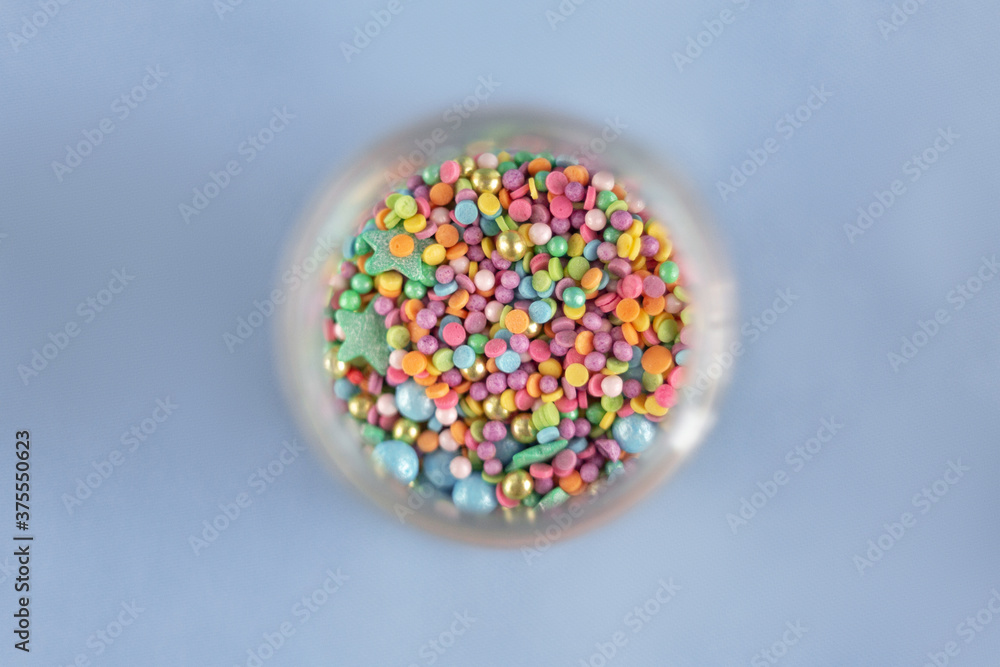 Top view on a colorful confectionery sprinkling in glass jar, decoration for cake and bakery on blue background Top view on a colorful confectionery sprinkling in glass jar, decoration for cake and bakery on blue background
