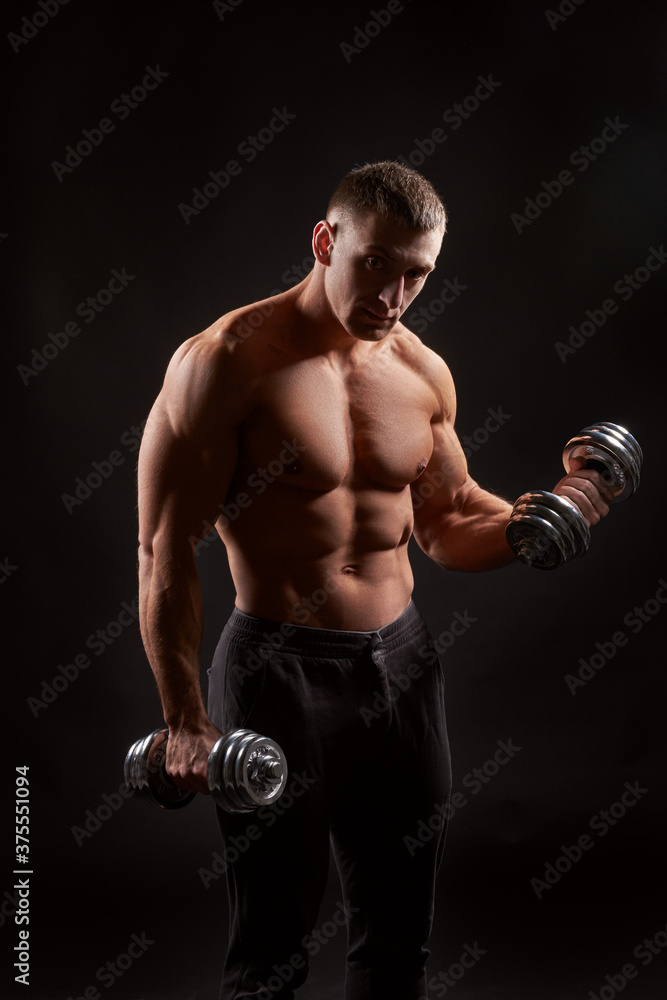 Shirtless muscular man holding dumbbells against of black background.Studio shot Shirtless muscular man holding dumbbells against of black background.Studio shot