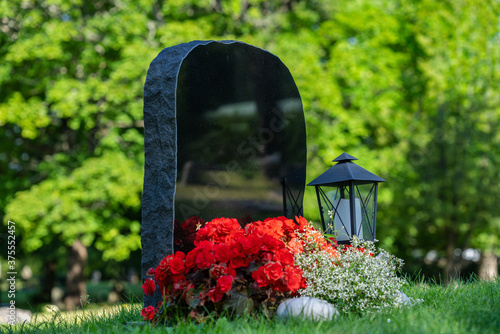 Fotografia Black gravestone with red and white flowers and without name inscription, on a w