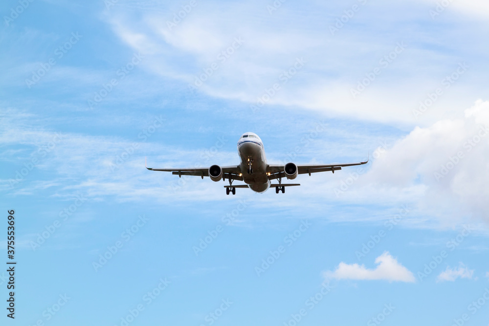 white passenger plane comes in to land with natural background of white clouds and blue sky
