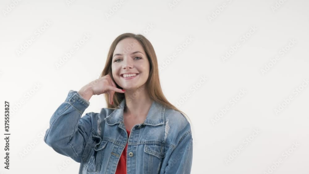 A young blonde woman looks at the camera and shows a call me gesture. White background. A young blonde woman looks at the camera and shows a call me gesture. White background.
