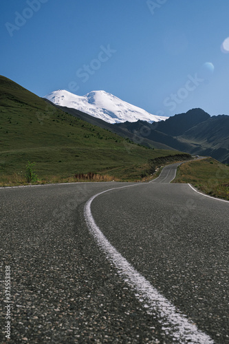 An asphalt road leading to the mountains. Picturesque landscape. Postcard