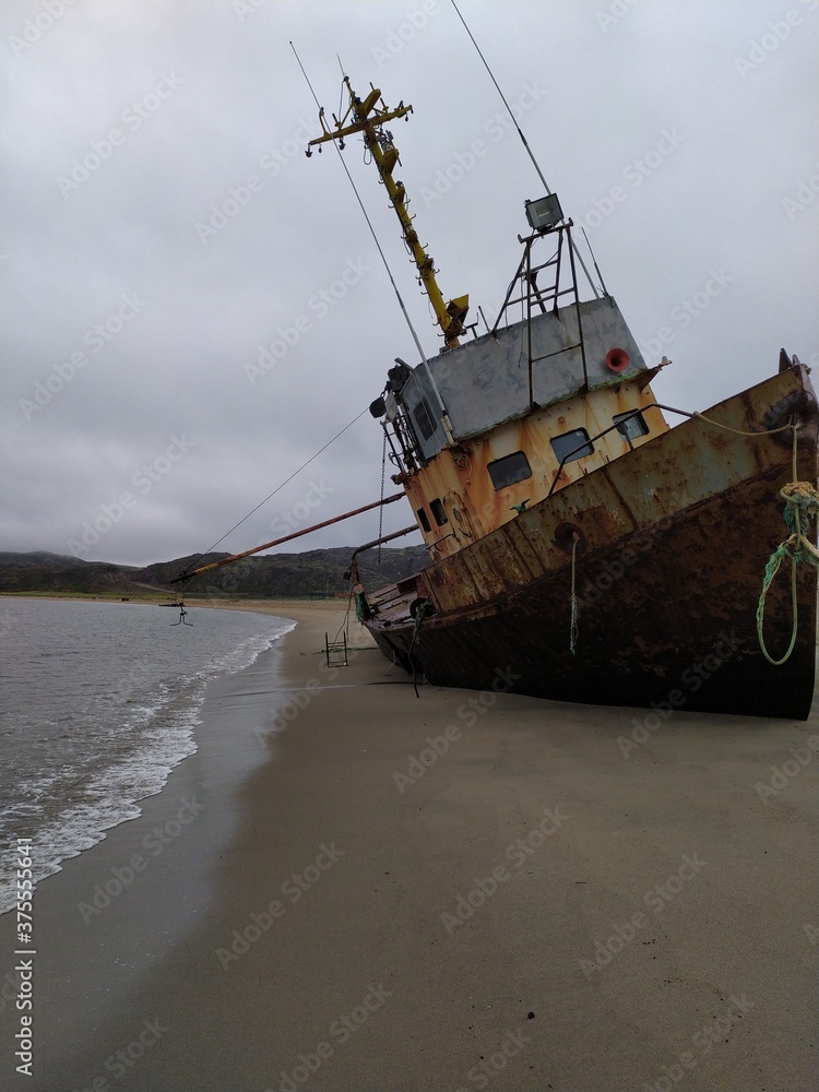 Old abandoned rusty metal ship on the sandy shore of the barents sea