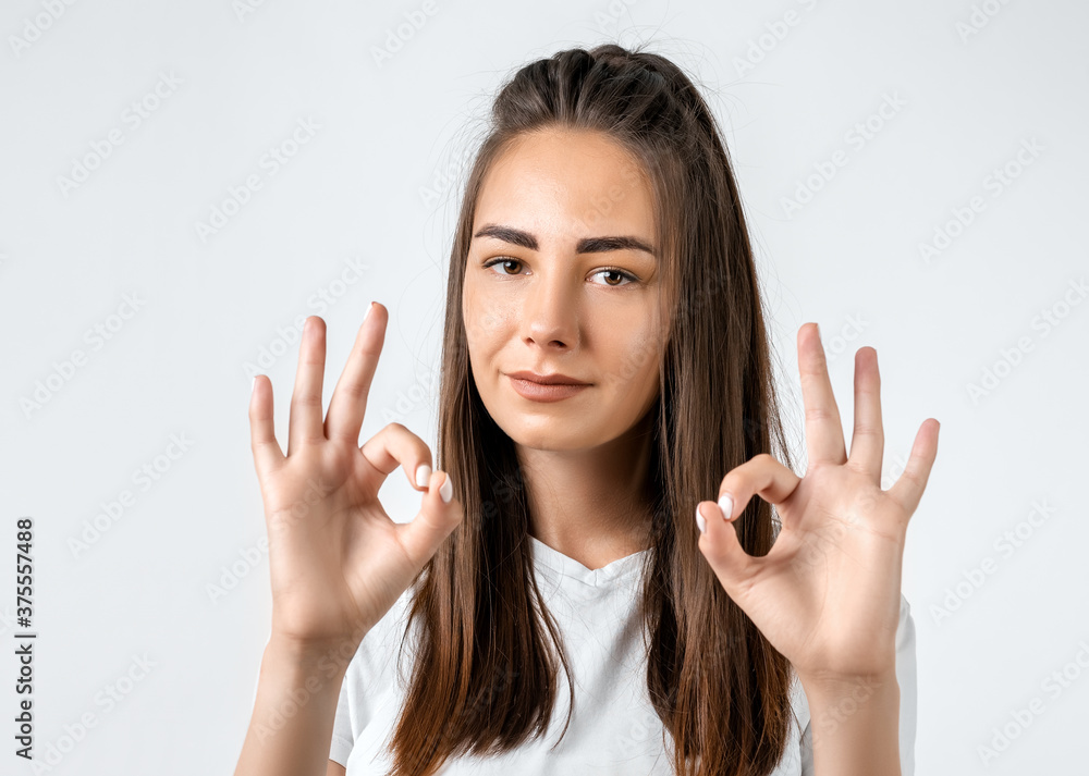 Modern girl with long chestnut hair making OK with both hands, gesture as if saying that everything is fine Modern girl with long chestnut hair making OK with both hands, gesture as if saying that everything is fine