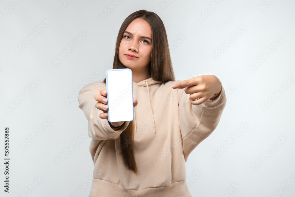 Portrait of pretty girl pointing finger at blank screen mobile phone isolated over white background Portrait of pretty girl pointing finger at blank screen mobile phone isolated over white background