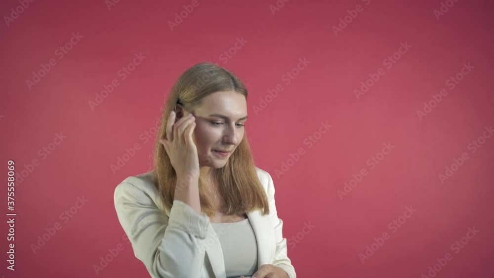 Portrait of a young beautiful brunette woman looking at the camera smiling and flirting. An embarrassed look. Pink background. Portrait of a young beautiful brunette woman looking at the camera smiling and flirting. An embarrassed look. Pink background.