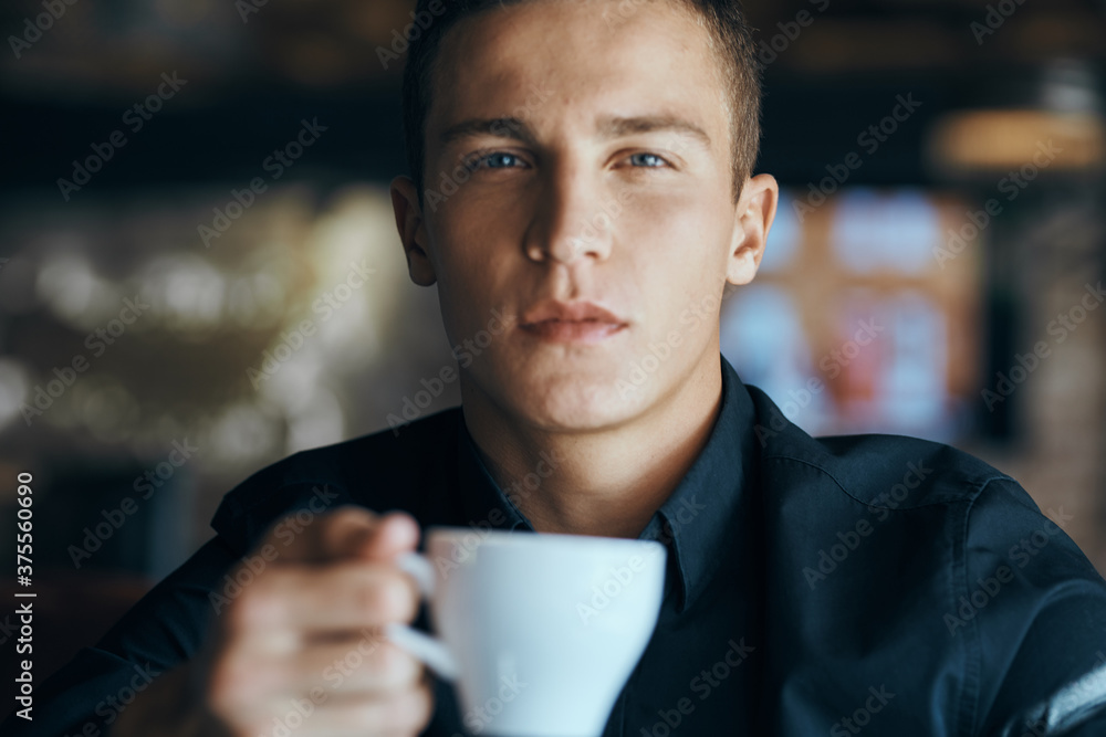 Businessman with a cup of coffee in a cafe and a dark shirt handsome face Businessman with a cup of coffee in a cafe and a dark shirt handsome face
