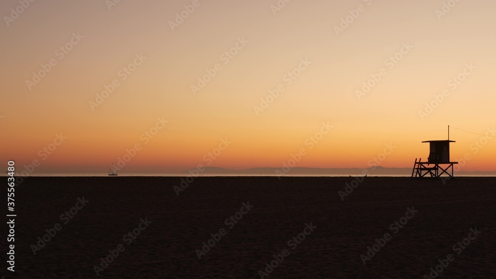 Summertime travel concept. Dark silhouette, iconic retro wooden lifeguard watch tower against sunset orange sky. Contrast watchtower outline, california pacific ocean beach twilight aesthetic, CA USA
