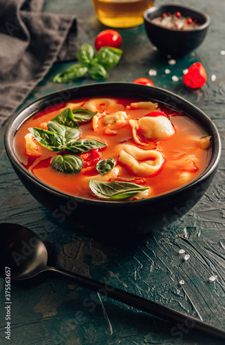Tomato soup with tortellini in black bowl on dark background.