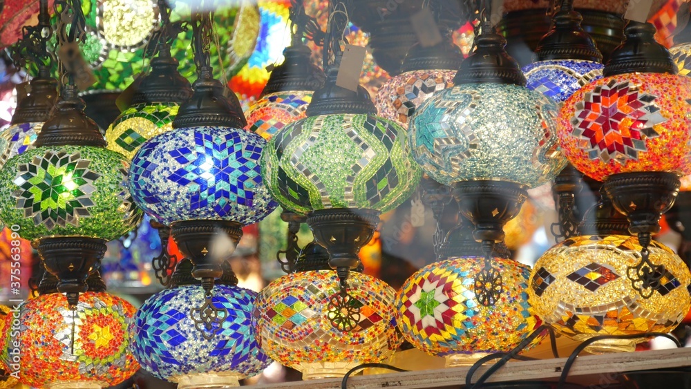 Colourful turkish lamps from glass mosaic glowing. Arabic multi colored authentic retro style lights. Many illuminated moroccan craft lanterns. Oriental islamic middle eastern decor. Shiny folk shop