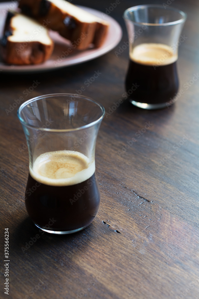 .Two glasses of espresso on a wooden table with pieces of cake on a plate. .Two glasses of espresso on a wooden table with pieces of cake on a plate.