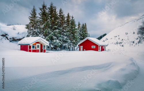 Traditional Norwegian red wooden houses under the fresh snow. Fabulous winter scene of Lofoten islands on the shore of Kongsjordpollen fjord, Vestvagoy, Norway, Europe. Life over polar circle.