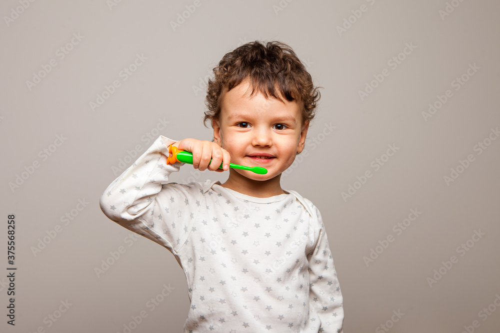 funny curly kid stands smiling and holds a toothbrush in his hands. Healthy strong children's teeth. The rules of personal hygiene. white background, isolated funny curly kid stands smiling and holds a toothbrush in his hands. Healthy strong children's teeth. The rules of personal hygiene. white background, isolated
