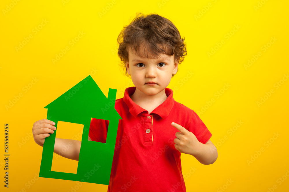 The boy points his finger at the green layout of the house. The child in the red shirt shows the finger that you need to stay at home. On a yellow background The boy points his finger at the green layout of the house. The child in the red shirt shows the finger that you need to stay at home. On a yellow background