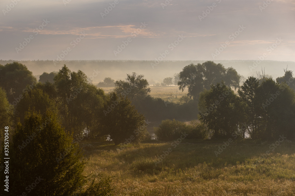 Amazing scenic early morning misty landscape just before sunrise. Aerial view photography of orange sky, horizon line, meadows and forests covered with thick white fog.