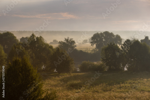 Amazing scenic early morning misty landscape just before sunrise. Aerial view photography of orange sky, horizon line, meadows and forests covered with thick white fog.