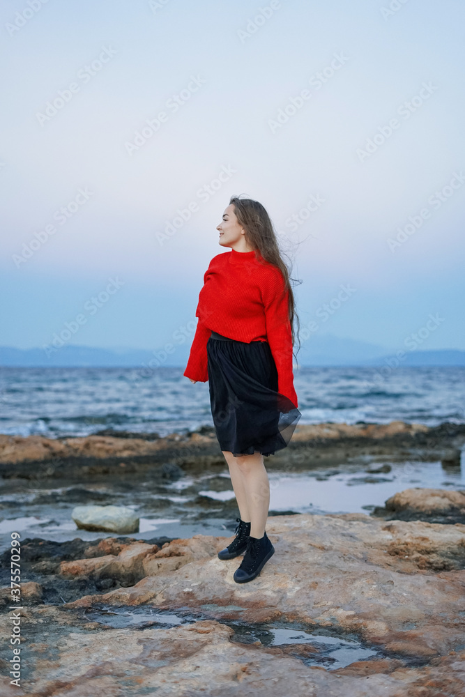 Portrait of a happy joyful woman wearing a red sweater in the beach in a cloudy windy evening near the sea